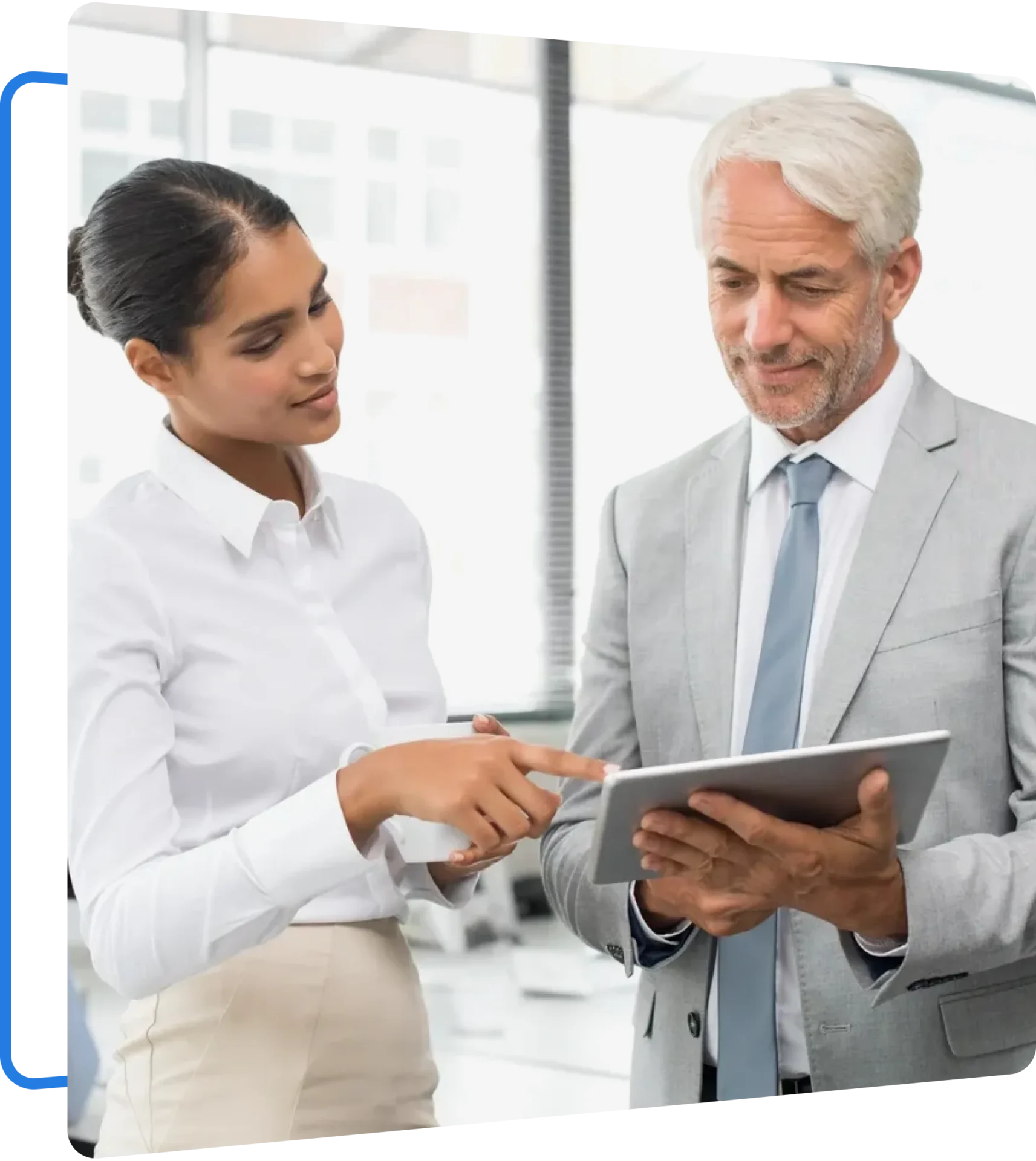 Group 5 A woman in a white blouse and a man in a gray suit discuss something on a tablet in an office setting.